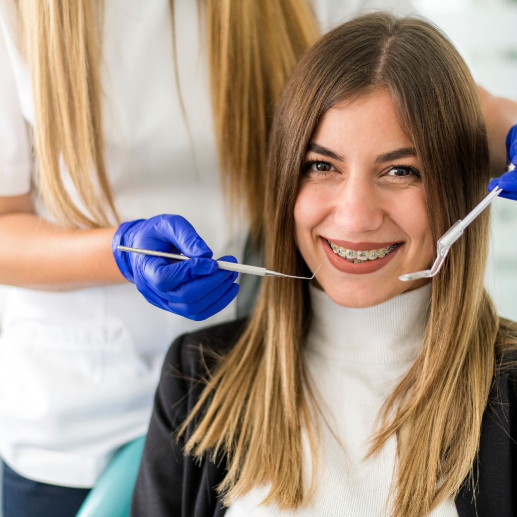 imagem de jovem mulher a sorrir para a câmara com aparelho fixo e mão de dentista prestes a fazer exame oral