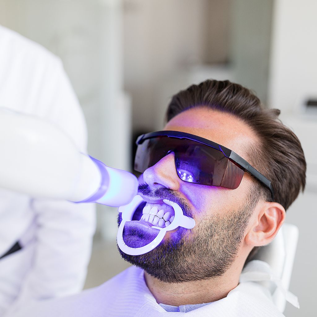 imagem de homem jovem paciente com óculos de protecção enquanto é efectuado tratamento de branqueamento dentário