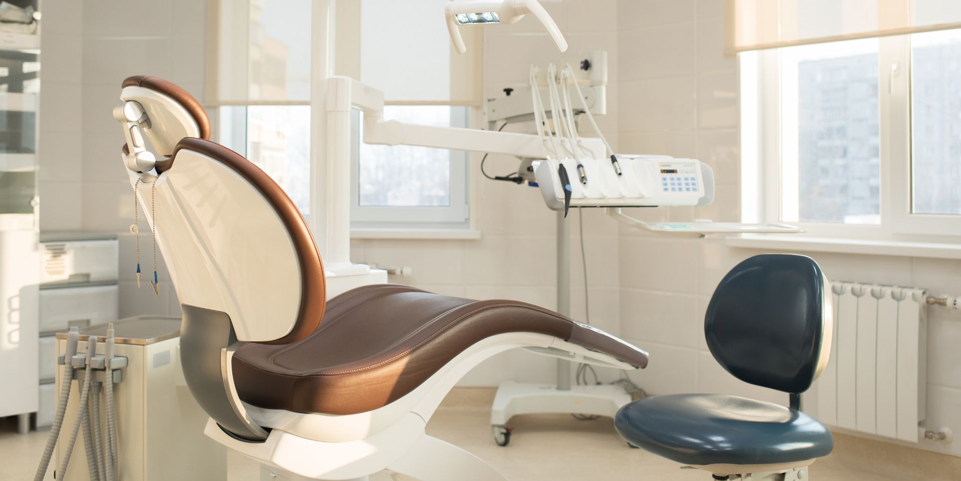 imagem de consultório de dentista bem iluminado por luz natural com cadeira para pacientes em castanho e branco