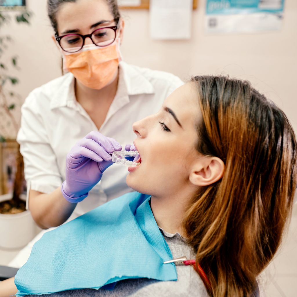 imagem de dentista a auxiliar a aplicação de alinhador invisalign na boca de paciente