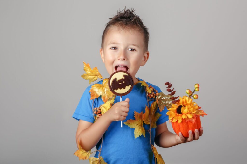imagem de menino feliz com camisola azul a comer um doce de halloween com um morcego e uma abóbora na outra mão