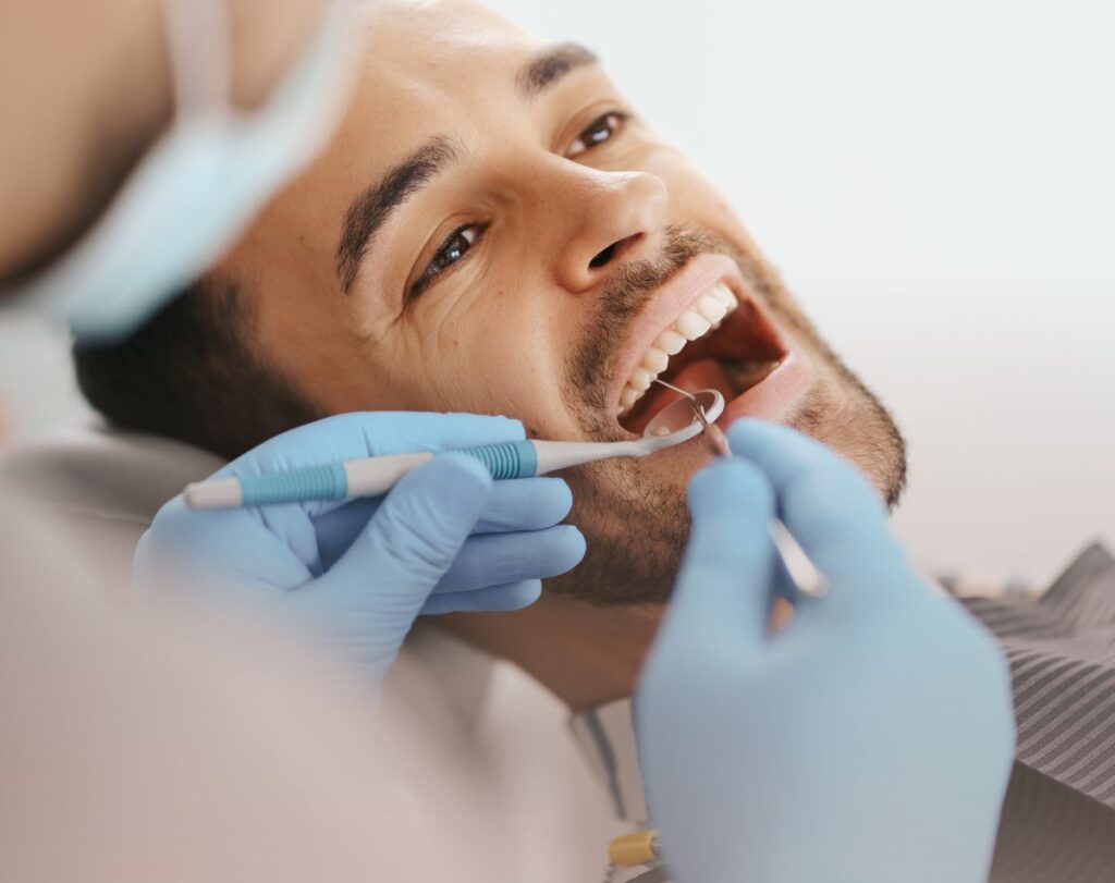imagem de homem sentado na cadeira do dentista com a boca aberta e a ser tratado por um dentista